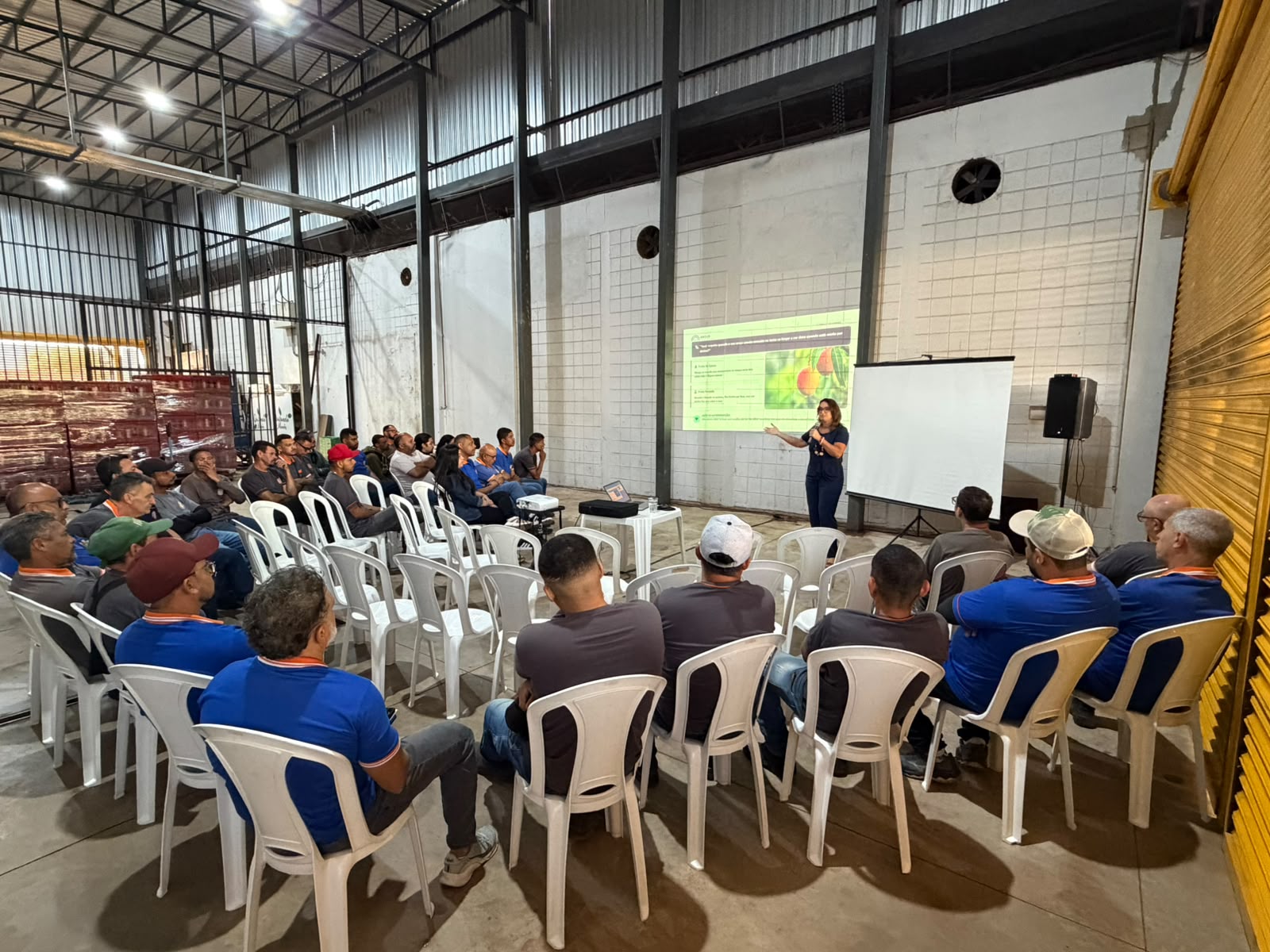 Psicóloga explicando o slide sobre fruta de época e fruta forçada para a equipe da Comercial Mendes